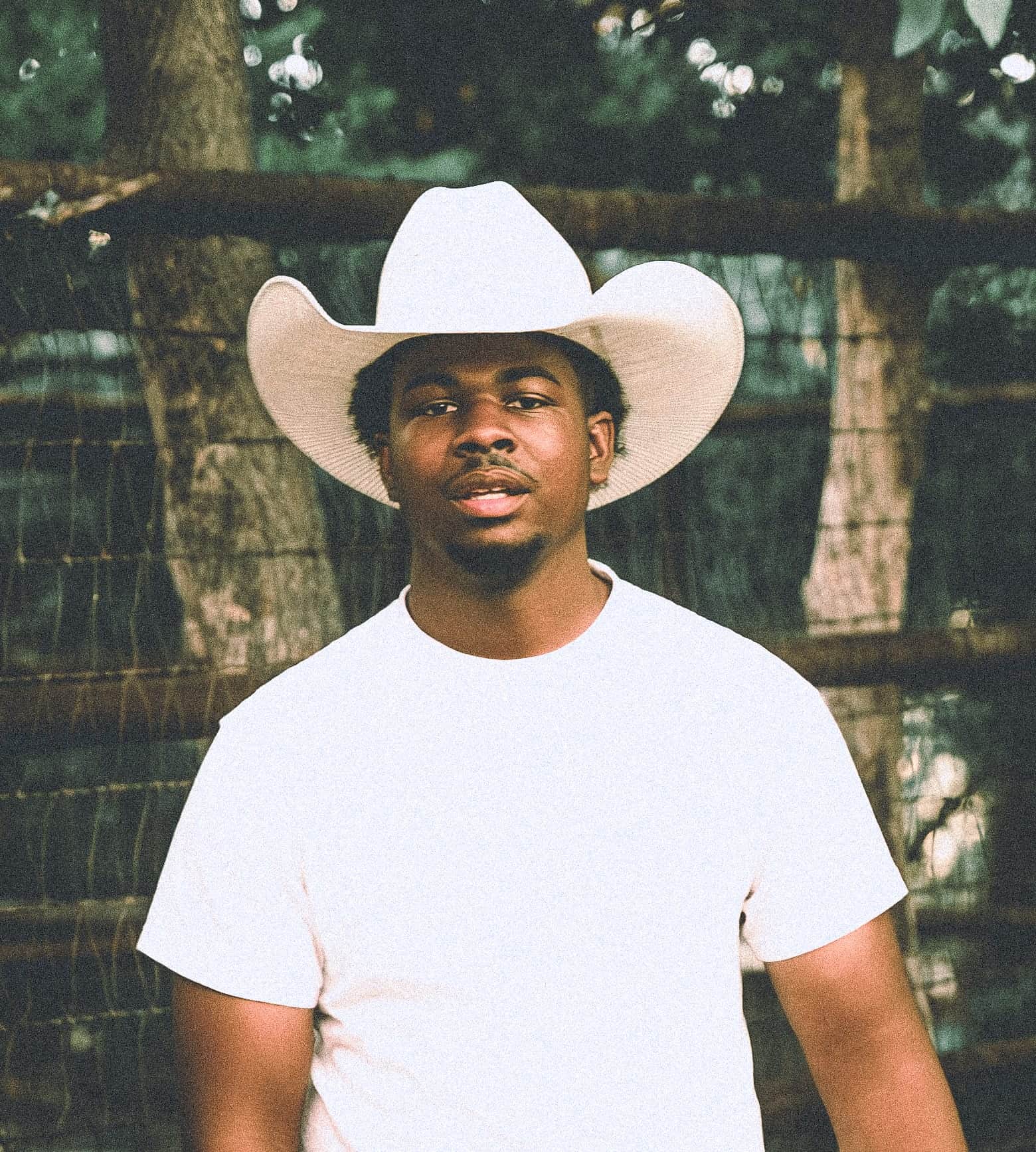 Portrait of Luhdeeskii in a white cowboy hat against a wire fence